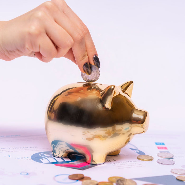A hand places a coin into a golden piggy bank surrounded by financial documents, symbolizing savings.