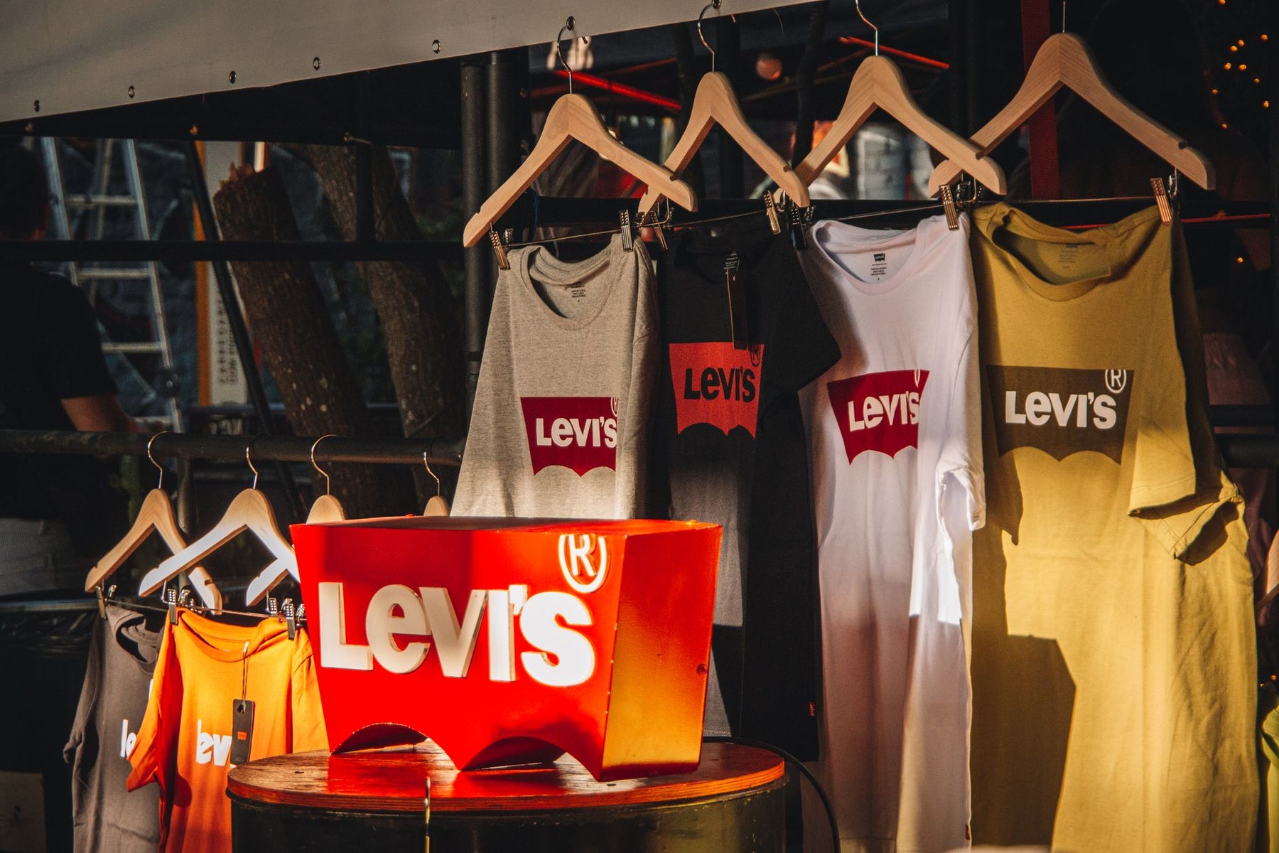 Vibrant display of Levis T-shirts hanging on wooden hangers in a sunlit store.