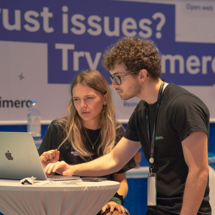 Two individuals collaborating on a laptop at a tech conference booth promoting Calimero.