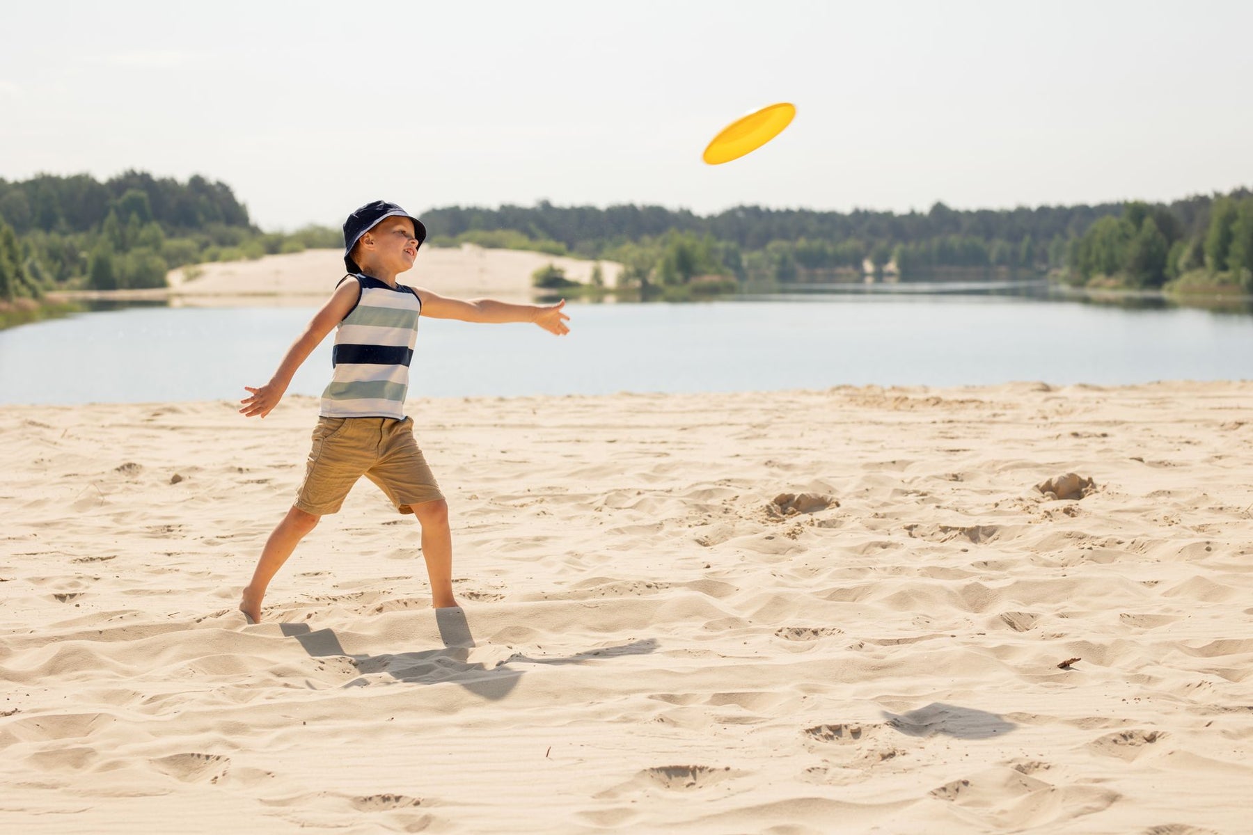 A boy having fun throwing a frisbee on a sunny sandy beach by a lake.