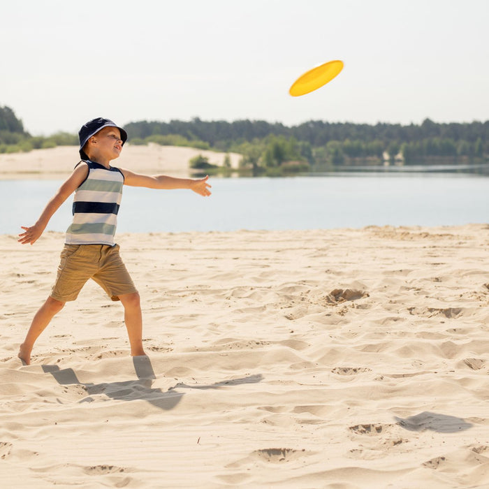 A boy having fun throwing a frisbee on a sunny sandy beach by a lake.