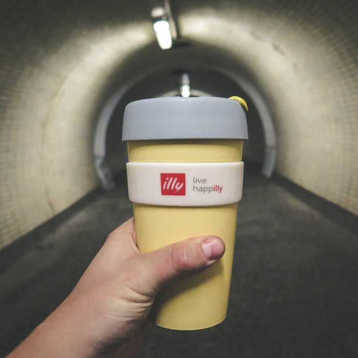 Perspective shot of a hand holding a reusable coffee cup inside a dimly lit tunnel.