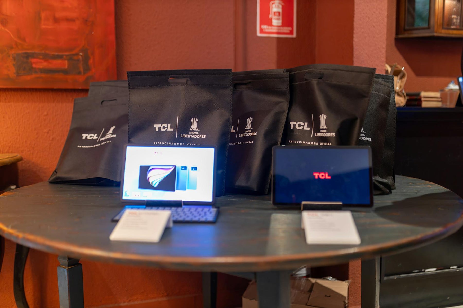 A promotional setup showcasing TCL tablets and branded gift bags on a round table indoors.