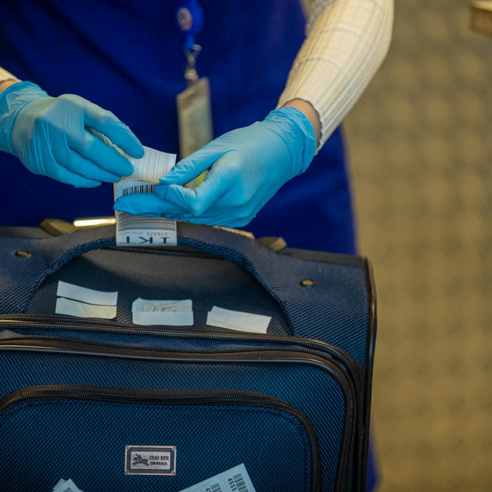 Close-up of airport security process with gloved hands inspecting luggage tags.