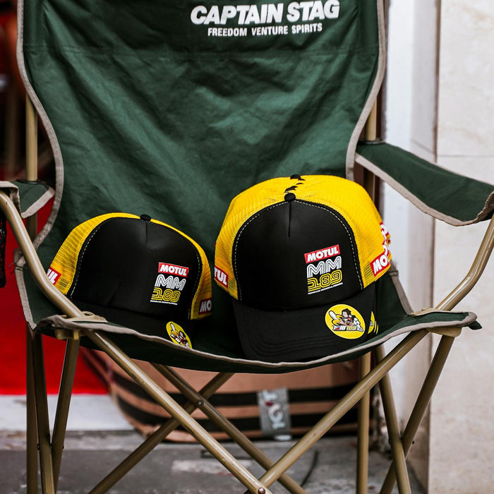 Black and yellow caps with Motul branding on a green foldable chair indoors.