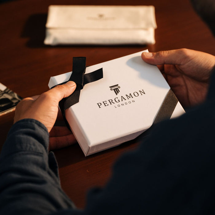 Hands holding a Pergamon London gift box on a wooden table, creating an elegant unboxing theme.