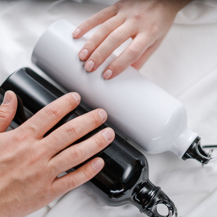 Close-up of hands holding reusable black and white tumblers on a white surface.