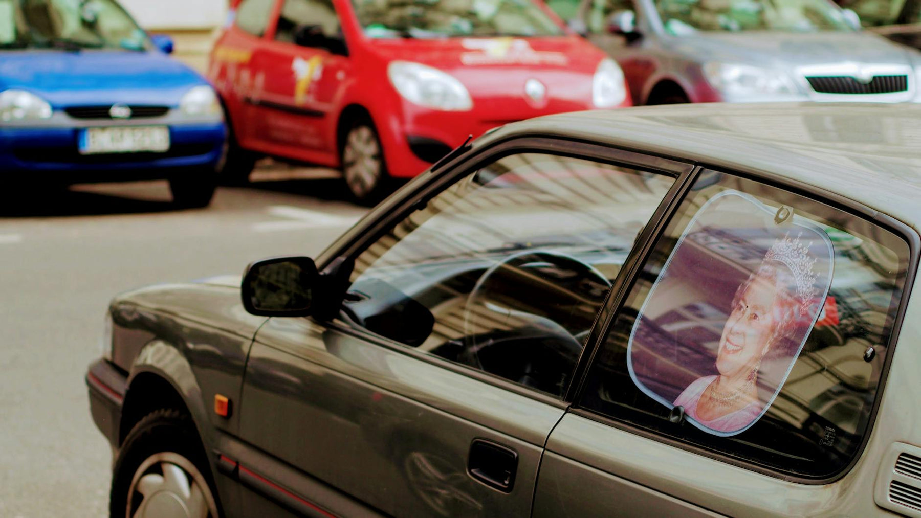 A close-up of cars parked on the street featuring a decorative sunshade with a royal image.