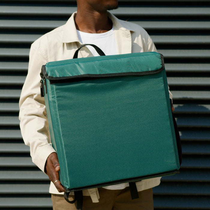 Delivery worker holding a large green insulated package outside a building with metal shutters.