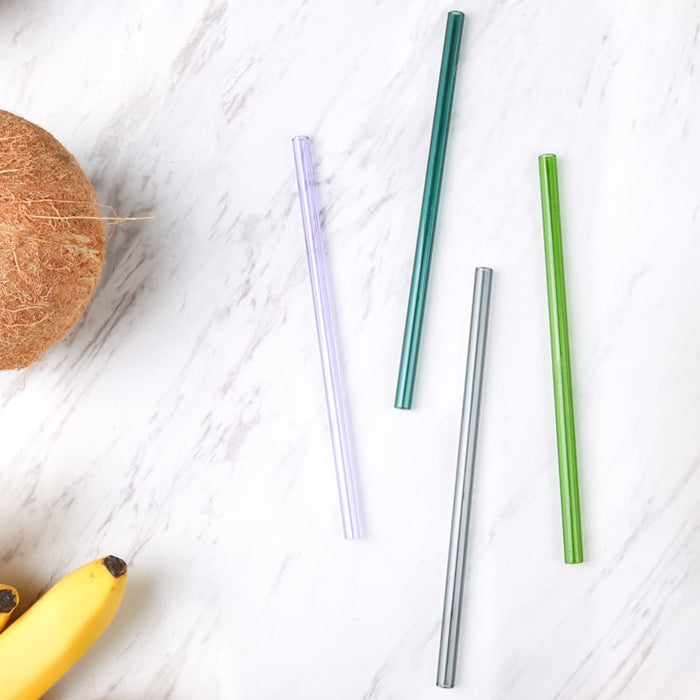 four assorted-color straws beside coconut, bananas, and pineapple