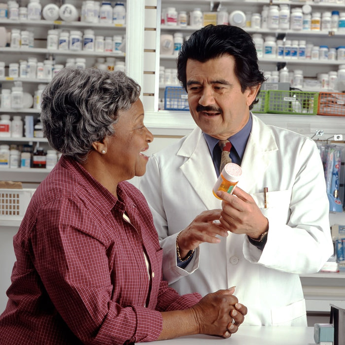 A pharmacist in a white coat showing a pill bottle to a woman