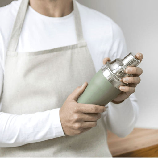 Seasons Gaudie Recycled Stainless Steel Cocktail Shaker - A stainless steel cocktail shaker in matte green, held by a person wearing an apron, with a silver top.