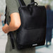Moleskine Metro Slim Backpack - A black Moleskine Metro Slim Backpack is worn on a person's back, featuring a sleek design and a branding logo.