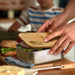 NATURA Stainless Steel Lunch Box - A stainless steel lunch box with a bamboo lid, filled with sandwiches and greens, on a wooden surface.
