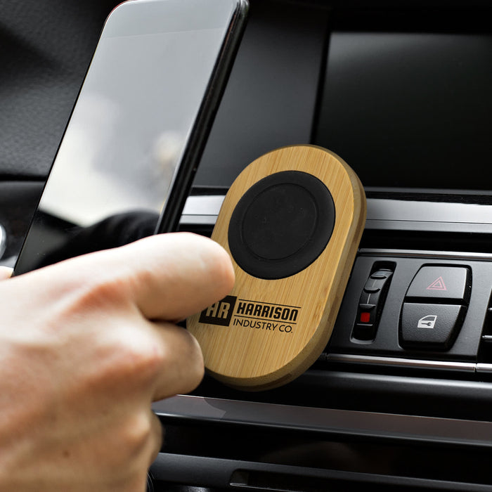 Bamboo Car Phone Holder - A bamboo car phone holder with a black circular grip, placed in a car dashboard vent, holding a smartphone.