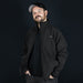 Swiss Peak Urban Softshell Jacket - A man wearing a black Swiss Peak Urban Softshell Jacket with a logo, against a dark background.