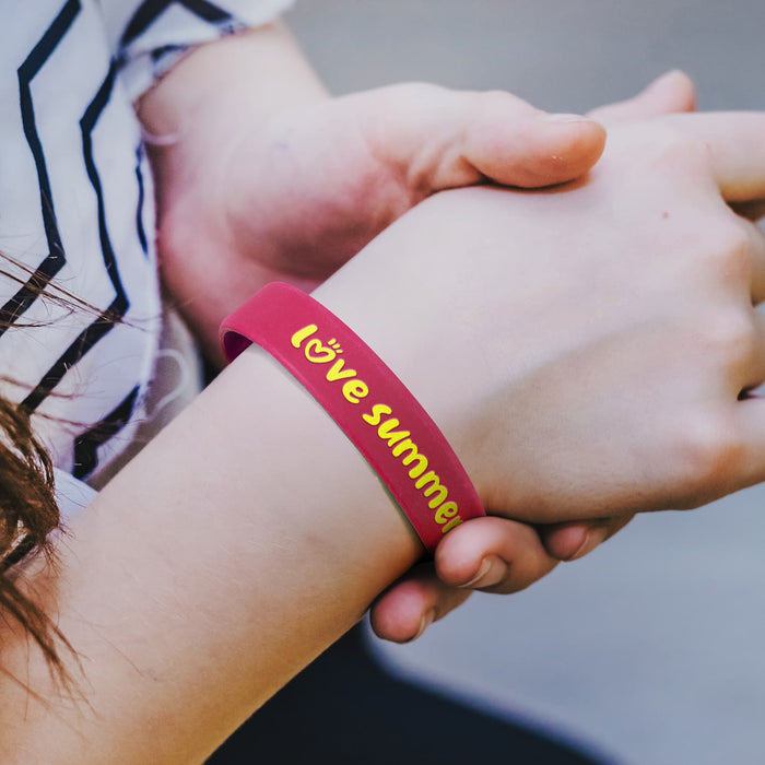 Kids Silicone Wrist Band - Embossed - A pink silicone wristband with embossed text and a logo, worn on a person's wrist.