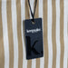 Keepsake Beach Tote Bag - A striped beach tote bag in cream and tan, featuring a tag with a logo attached.
