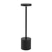 Nouveau Rechargeable Table Lamp - A black rechargeable table lamp with a cylindrical base and a flat, circular top. It features a simple, modern design.