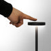 Nouveau Rechargeable Table Lamp - A hand touching the top of a sleek, black rechargeable table lamp with a minimalistic design.