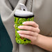 Neoprene Cup Sleeve - Medium - A drink bottle covered with a green neoprene sleeve featuring lime and olive designs, held in a person's hand.