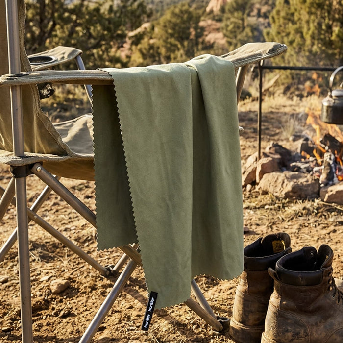 Frontier Rapid Dry Towel - A green Frontier Rapid Dry Towel hangs from a camping chair beside a fire, with boots on the ground nearby.
