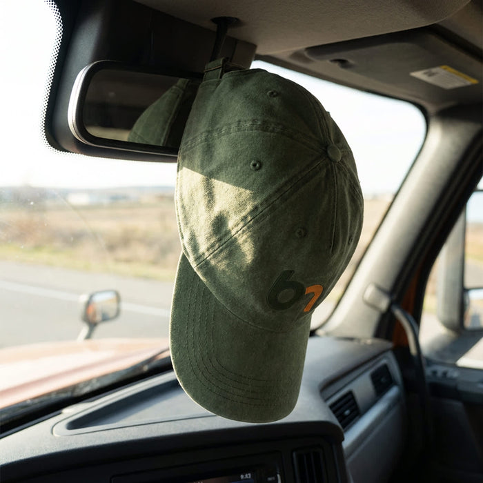 Vintage Washed Cap - A green vintage washed cap hanging from the mirror inside a vehicle, with a logo on the front.