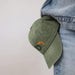 Vintage Washed Cap - A vintage washed cap in olive green, featuring a small logo, hanging from a denim pocket.
