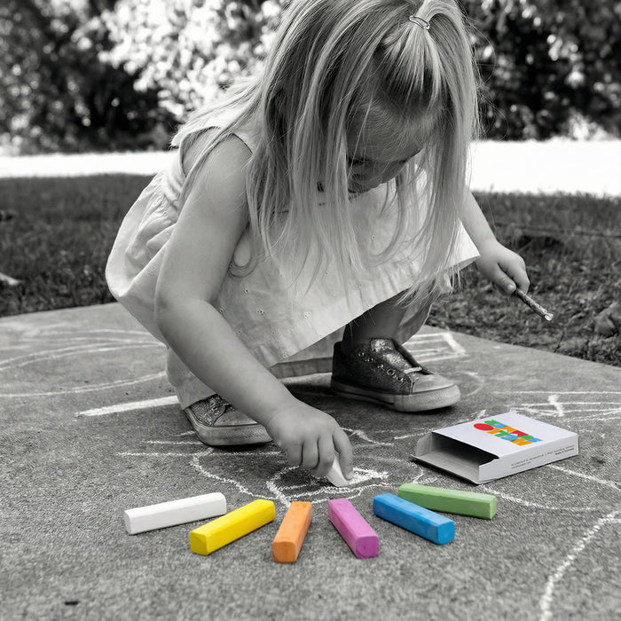 STAEDTLER Assorted Sidewalk Chalk Set - A child uses colourful chalk sticks, including white, orange, pink, green, and purple, from an open box on the ground.