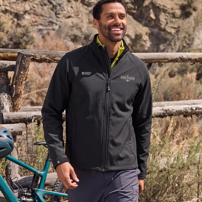 Swiss Peak Urban Unisex Softshell Jacket - A unisex softshell jacket in black, featuring a logo, worn by a smiling individual outdoors.