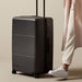 Kadi Check-In Suitcase - Large - A large black suitcase on wheels with a retractable handle and a logo.