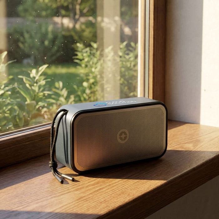 Swiss Peak 10W Bass Speaker - A grey Bluetooth speaker sits on a windowsill, showcasing a sleek design with a logo on its front.