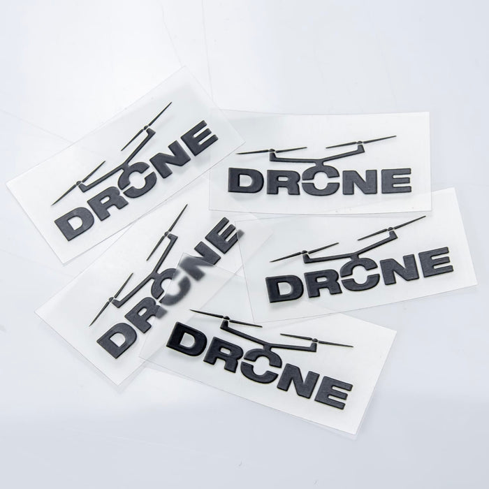 Prism Print - 40 x 20mm Sticker - Four black "DRONE" stickers on a clear backing, arranged on a light grey surface.
