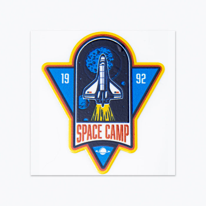 Prism Print - 50 x 50mm Sticker - A colourful sticker depicting a space shuttle with the text "Space Camp" and a retro design featuring blue and orange accents.