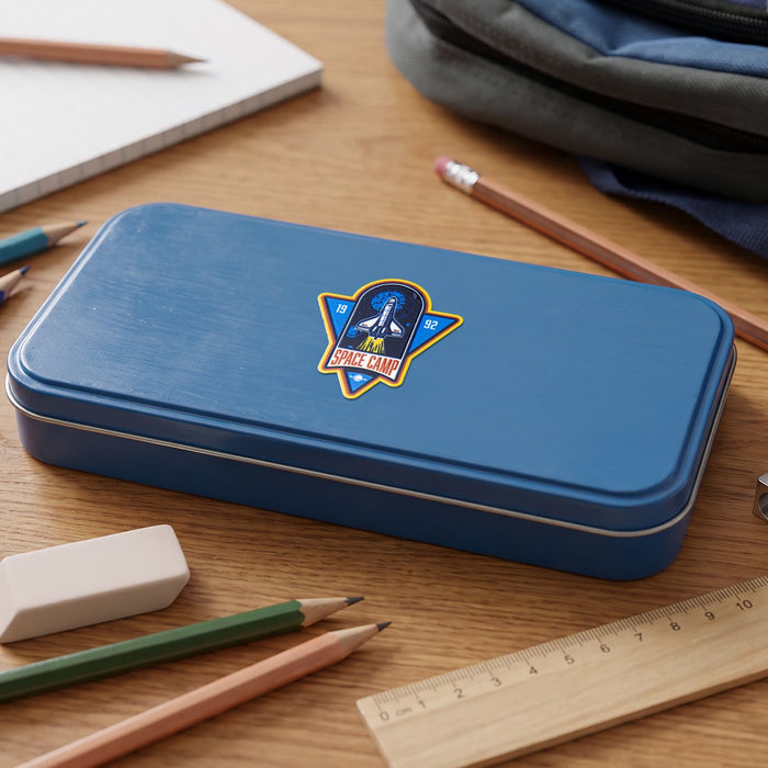 Prism Print - 50 x 50mm Sticker - A blue pencil case with a logo sits on a wooden desk surrounded by pencils, an eraser, a ruler, and a notebook.