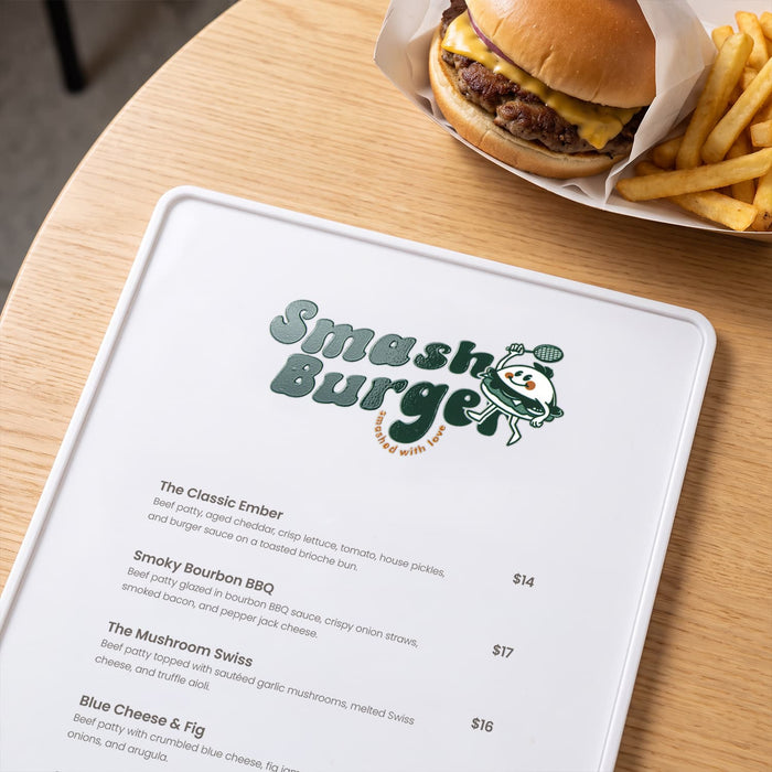 Prism Print - 100 x 50mm Sticker - A menu on a wooden table featuring various burger options alongside a cheeseburger and fries in the background.