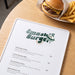 Prism Print - 100 x 50mm Sticker - A menu on a wooden table featuring various burger options alongside a cheeseburger and fries in the background.