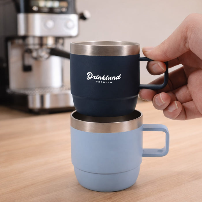 Stackable Stainless Steel Mug - A stackable stainless steel mug set in navy and light blue, featuring a handle and a logo, displayed on a wooden surface.