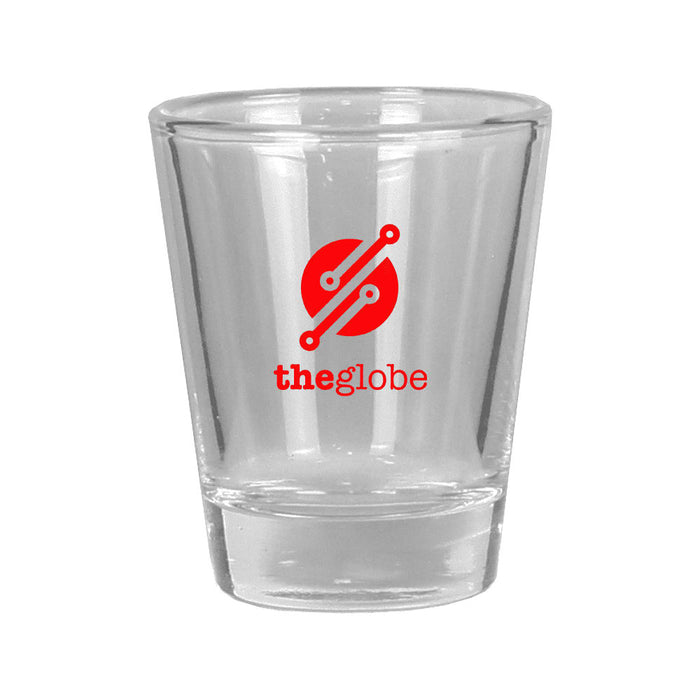 Shot Glass - A clear glass shot glass with a solid base and a round logo in red and white.