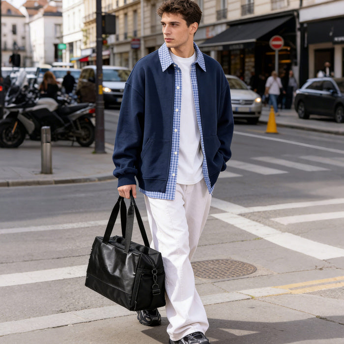 Carry-on Duffle Bag - A person in a navy jacket and white pants carries a black leather carry-on duffle bag while walking on the street.