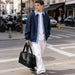 Carry-on Duffle Bag - A person in a navy jacket and white pants carries a black leather carry-on duffle bag while walking on the street.