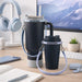 Silicone Cup Carry Strap - A drink bottle carrying two silicone cup carry straps in black and light blue, placed on a desk with headphones and stationery.