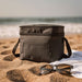 Tundra GRS RPET Double Compartment Cooler Bag 13L - A grey double compartment cooler bag sits on sandy beach alongside sunglasses and a towel, with ocean waves in the background.