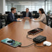 10000mAh Power Bank with Charging Cable - A 10000mAh power bank in black with connected charging cables, alongside two smartphones and a pair of earbuds on a conference table.