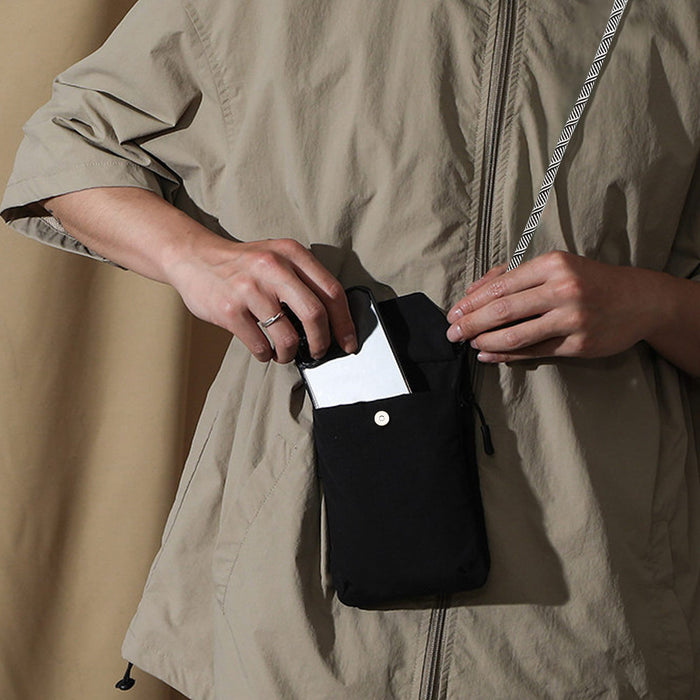 Minimalist Crossbody Phone Bag - A minimalist black crossbody phone bag being held by a person, with a phone partially inserted into its pocket.