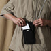Minimalist Crossbody Phone Bag - A minimalist black crossbody phone bag being held by a person, with a phone partially inserted into its pocket.