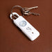 Safety Alarm Keychain - A white safety alarm keychain with a circular light, attached to a set of silver keys on a brown leather surface.