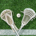 Lacrosse Ball - A white lacrosse ball positioned between two white lacrosse sticks on artificial grass.