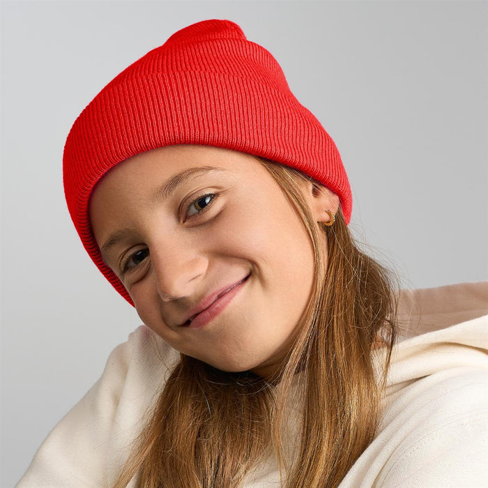 Kid Wind-S Beanie - Recycled Polyester - A red knitted beanie worn by a child with long hair, featuring a logo on the side.