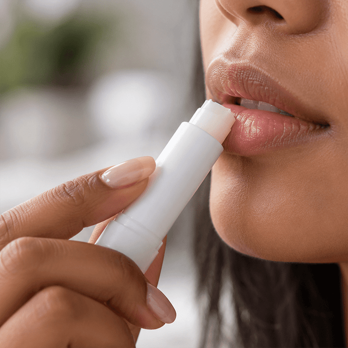 Twist Lip Balm - A twist lip balm in a white container being applied to lips. The person has light skin and natural-looking makeup.